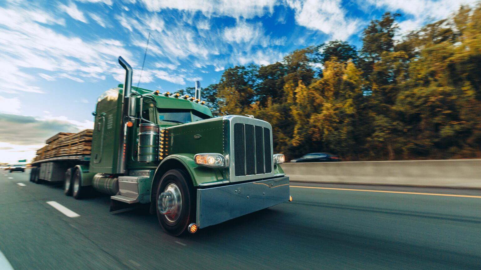 A large green semi-truck driving on a highway under a blue sky.