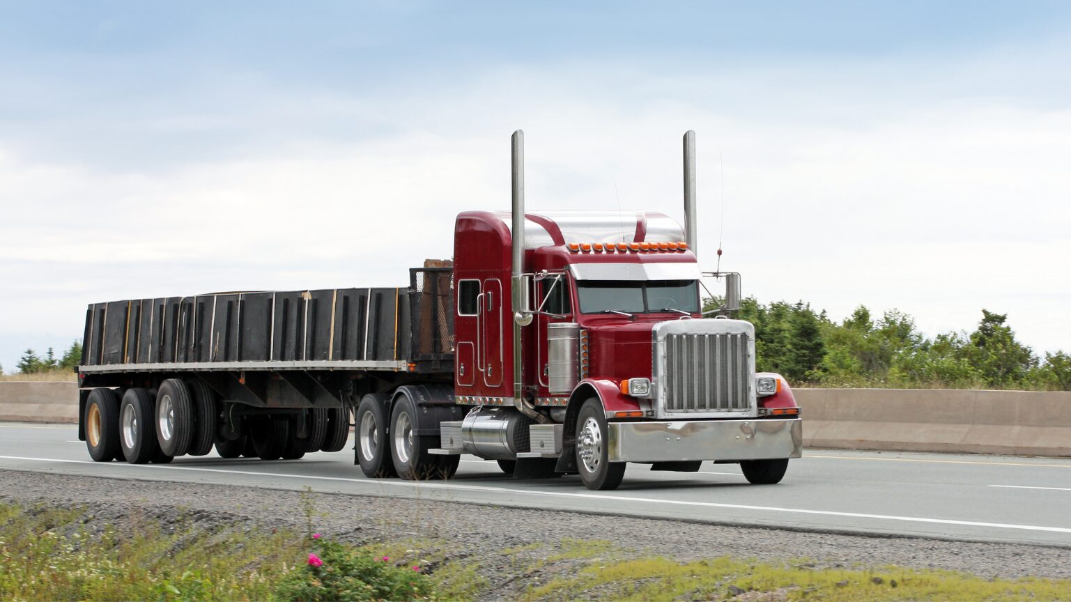A red semi-truck pulling a large trailer on a road.