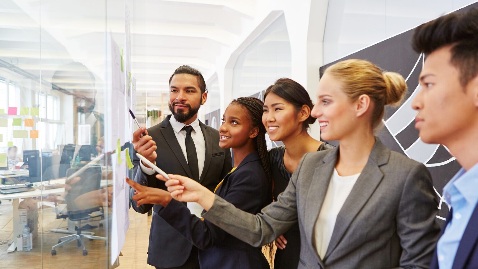 Four professionals collaborating with a whiteboard marker in a modern office.